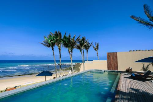 a swimming pool next to a beach with palm trees at Saline Taíba Boutique Beach Hotel in Taíba