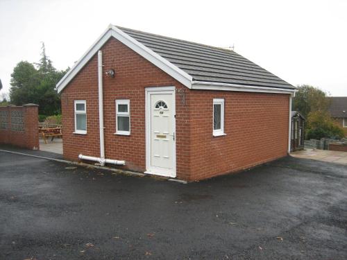 a small red brick building with a white door at Four seasons Guest House in Pembrey