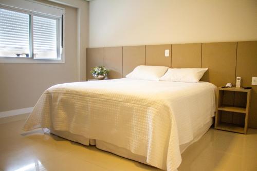 a bedroom with a large white bed with a window at Hotel Seville Comfort in Telêmaco Borba