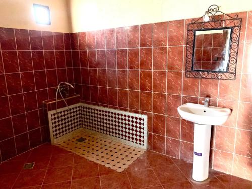 a brown tiled bathroom with a sink and a mirror at Maison Adrar Merzouga in Merzouga