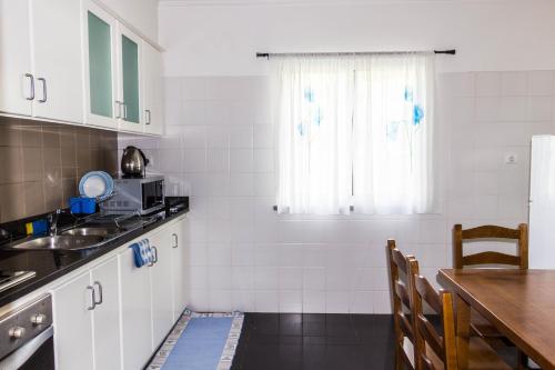 cocina con armarios blancos, mesa y ventana en Casa do Sol, en Ponta do Sol