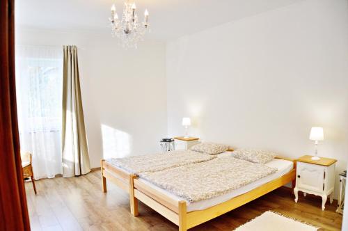 a white bedroom with a bed and a chandelier at R Cottage Jacuzzival in Balatonfenyves