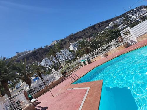 a large swimming pool next to a beach with palm trees at Cozy Apartment With Garden in Puerto Rico de Gran Canaria