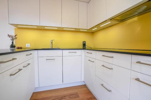 a kitchen with white cabinets and a yellow wall at Serenella Apartment in Riederalp