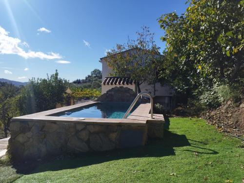 a swimming pool in a yard with a stone wall at Casa el Pino in Cortes de la Frontera