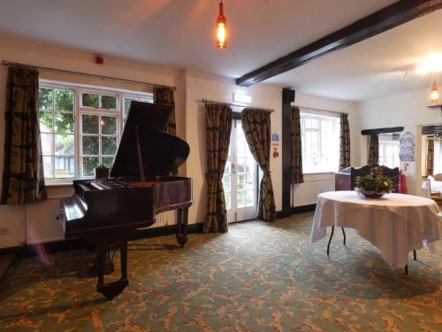 a room with a piano and a table and windows at Marston Farm Hotel in Sutton Coldfield