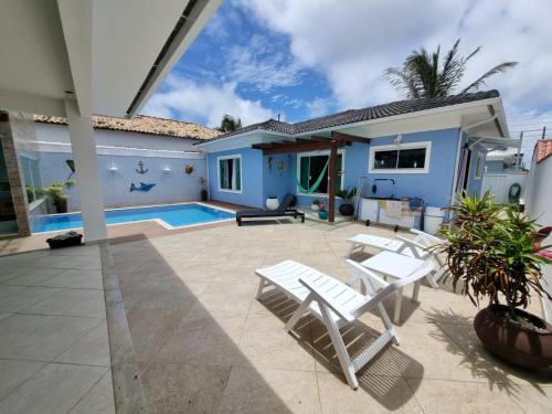 une terrasse avec des chaises blanches et une maison bleue dans l'établissement Casa Azul - Linda casa Familiar com Piscina no Peró em Cabo Frio, à Cabo Frio