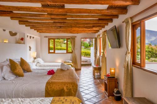 a bedroom with two beds and a tv and windows at Casa de Campo Hotel & Spa in Villa de Leyva