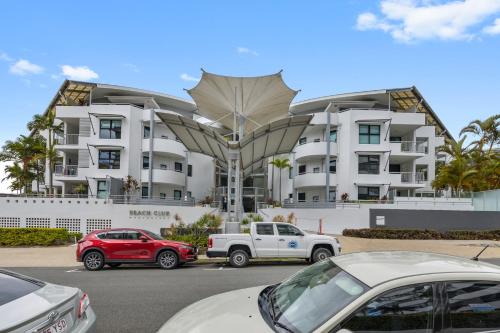 a large white building with cars parked in front of it at Beach Club Delight in Mooloolaba