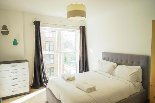LUXURY 2 BED WOOLWICH ARSENAL Apartment في لندن: غرفة نوم بسرير وملاءات بيضاء ونافذة
