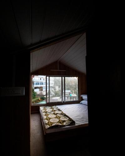 Bett in einem Zimmer mit einem großen Fenster in der Unterkunft MiakaHillsDarjeeling in Darjeeling