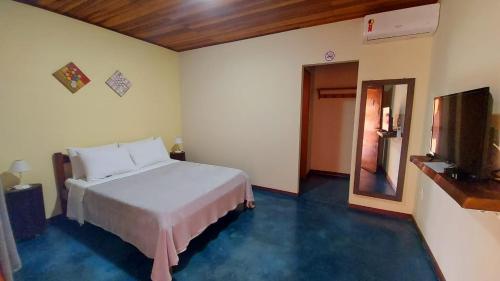 - une chambre avec un lit blanc et une télévision dans l'établissement Chalés Flor de Manacá, à Alto Paraíso de Goiás
