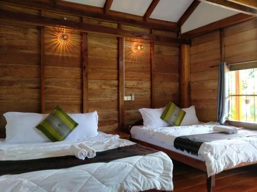 two beds in a room with wooden walls at The Hidden Oasis Bungalows in Kampot