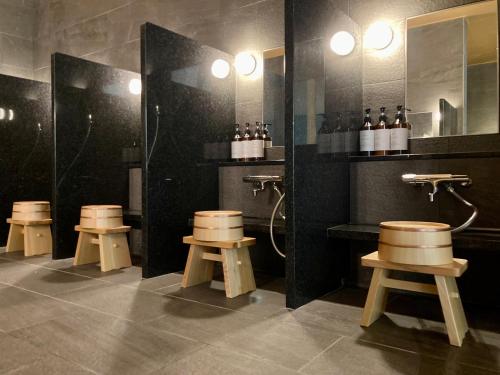 ein Badezimmer mit vier Hockern, einer Dusche und Spiegeln in der Unterkunft Urakusatsu TOU in Kusatsu