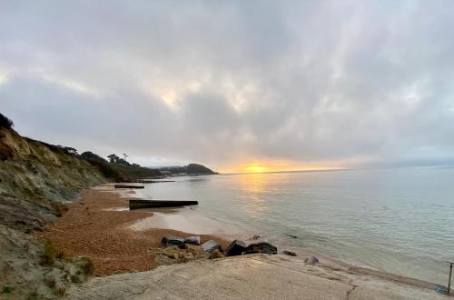 a beach with the sun setting over the water at SEAVIEW self-catering coastal bungalow in rural West Wight in Freshwater