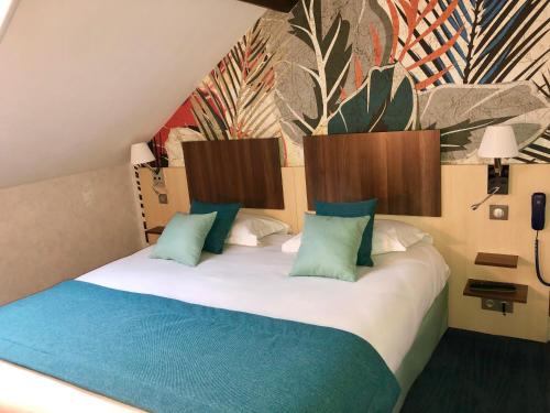 a bedroom with a large bed with green and blue pillows at HOTEL ARVERNA VICHY - ClT'HOTEL in Vichy