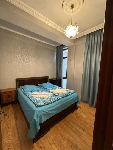 Schlafzimmer mit einem Bett mit blauer Bettwäsche und einem Kronleuchter in der Unterkunft Sun Apartment in Tbilisi City