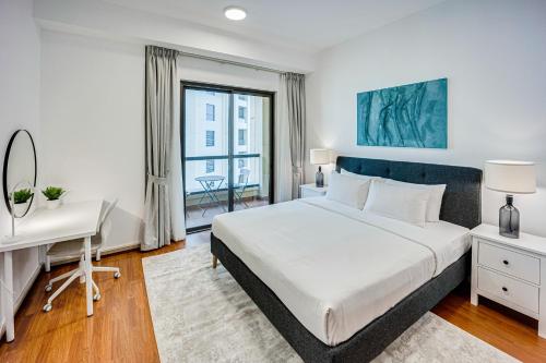 Un dormitorio con una cama blanca y un escritorio y una ventana. en Cozy 2 BD in Bahar JBR 24 floor, en Dubái