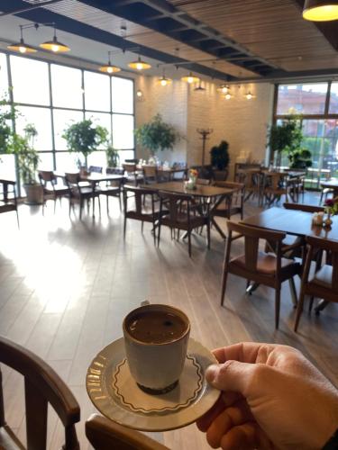 una persona sosteniendo una taza de café en un restaurante en Balıkesir Öğretmenevi, en Çayirhisar