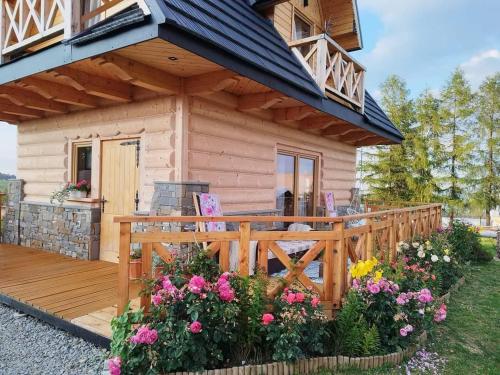 a small wooden cabin with a deck and flowers at Zymbiańsko Chałupa 1 z balią na wyłączność in Ząb