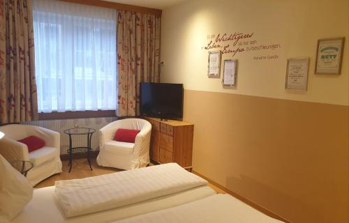 a hotel room with a bed and two chairs and a tv at Hotel Pension Alte Mühle in Klosterneuburg