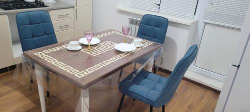 stół jadalny z 2 niebieskimi krzesłami oraz stół z kieliszkami do wina w obiekcie Квартира w mieście Atyrau