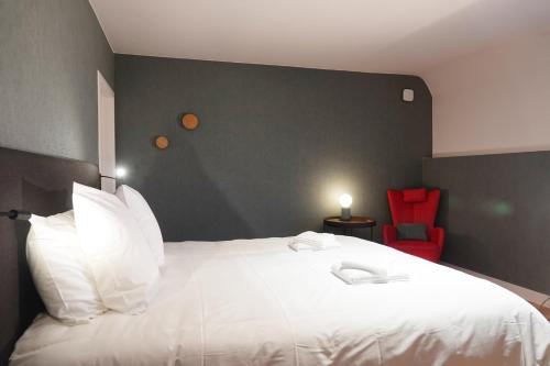 a bedroom with a large white bed with a red chair at Gîte XXV House - 8 personnes in Héron