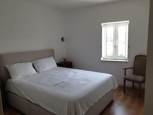 a bedroom with a white bed with a chair and a window at Casa do Moleiro in Mortágua