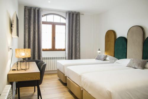 2 Betten in einem Zimmer mit einem Schreibtisch und einem Fenster in der Unterkunft Apartamentos Las Alas in Cartes