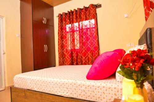 a bedroom with a bed with pink pillows and a window at Living Green APARTMENTS AIRPORT PICK UP in Benin City