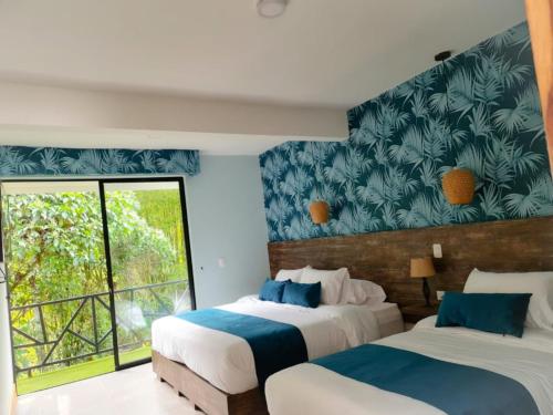 two beds in a room with a large window at Casa Hotel Bremen in Circasia