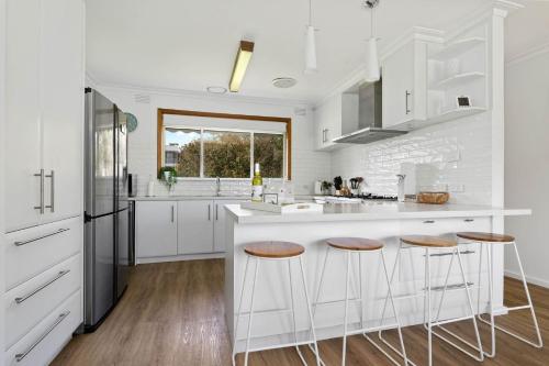 a kitchen with white cabinets and bar stools at Seaview Cottage and pool - Wifi and Linen included in Inverloch