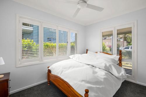 a bedroom with a bed with white sheets and windows at Tuncurry Close 1A in Nelson Bay