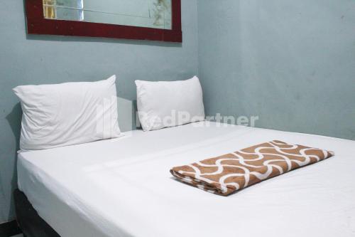 een wit bed met witte kussens en een deken erop bij Snow White Residence near Grogol Mitra RedDoorz in Jakarta