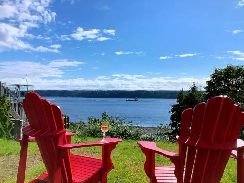 two red chairs sitting next to a table with a glass of wine at Ocean's Edge Suite in Campbell River