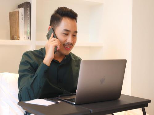 a man talking on a cell phone in front of a laptop at MORITZ INN BSD TANGERANG in Tangerang