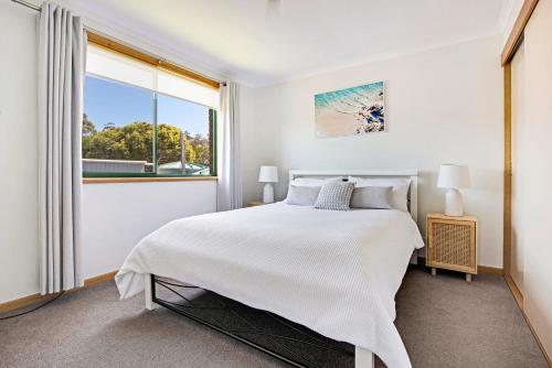 a white bedroom with a bed and a window at Bay of Fires Great Escape in Binalong Bay