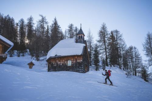 a man riding skis in the snow next to a cabin at Hotel Bergland in Sillian