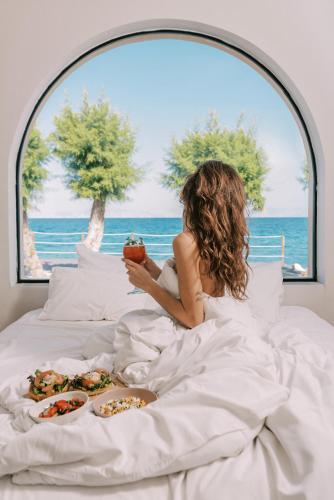 a woman laying in bed with food in front of a window at Villa Di Mare Seaside Suites in Ixia