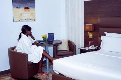 a woman sitting at a table with a laptop in a hotel room at New Heaven Hôtel in Yaoundé
