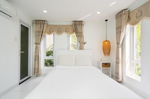 1 dormitorio con 1 cama blanca y 2 ventanas en Sunset Bãi Dâu Boutique Hotel Vũng Tàu, en Vung Tau