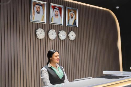 a woman sitting at a desk with clocks on the wall at Hotel Holiday International in Sharjah