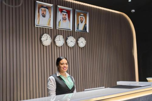 a woman standing in front of a counter with clocks at Hotel Holiday International in Sharjah
