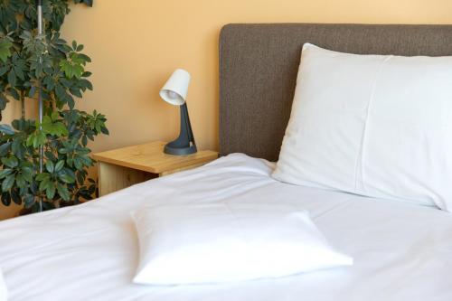 a bed with white sheets and a lamp on a night stand at Betli Panzió in Zalaegerszeg
