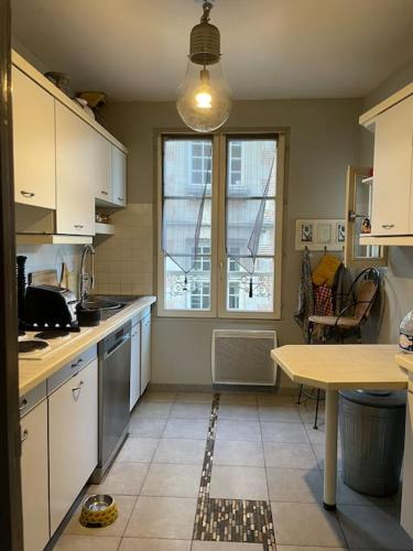 une cuisine avec des armoires blanches, une table et une fenêtre dans l'établissement Appartement sur le parvis de la cathédrale, à Senlis