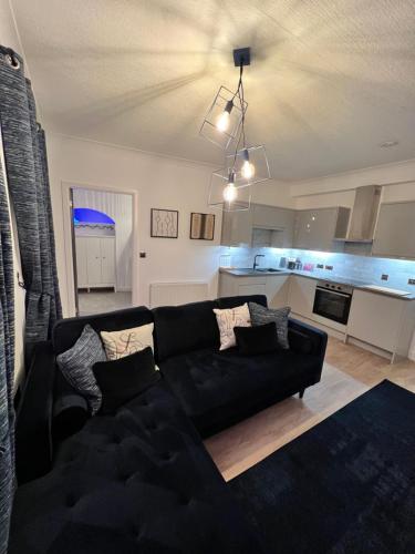 a living room with a black couch and a kitchen at Modern Town-Centre Apartment in Dumfries