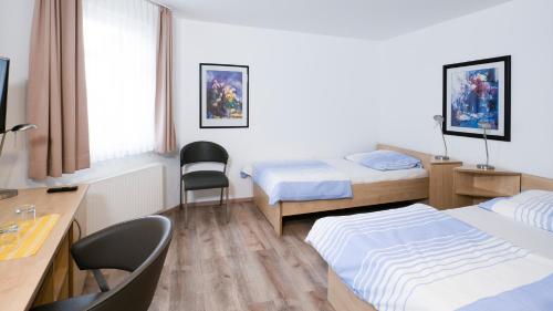 a room with two beds and a desk and a table at Brenzhotel Heidenheim in Heidenheim