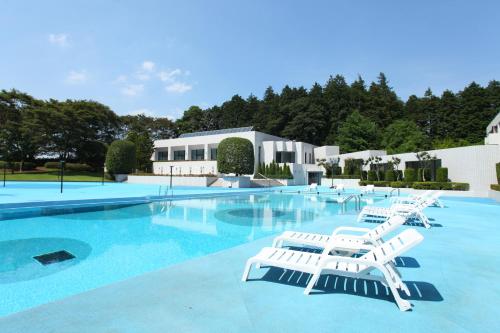 a swimming pool with white lounge chairs in front of a building at International Resort Hotel Yurakujo in Narita
