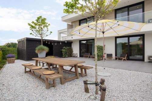 eine Terrasse mit einem Holztisch, Bänken und einem Sonnenschirm in der Unterkunft Hello Zeeland - Summum Suites in Domburg