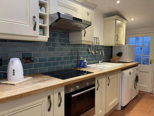 a kitchen with white cabinets and blue tiles on the wall at Smuggler's Cottage in Deal